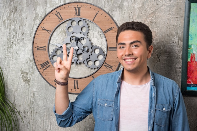 Free photo young man showing two fingers up and posing on marble background. high quality photo