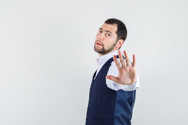 Young man showing wait gesture in shirt and vest and looking confident. .