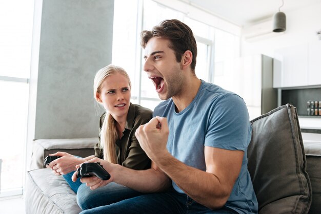Молодой человек показывая жест победителя пока играющ с его женщиной в видеоиграх