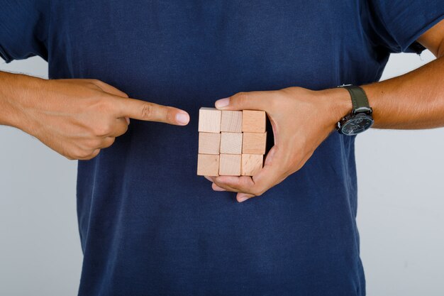 Young man showing wooden blocks in dark blue t-shirt front view.