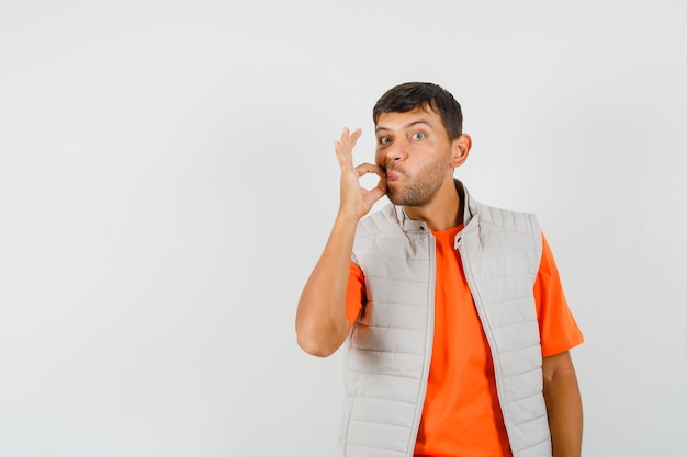 Young man showing zip gesture in t-shirt, jacket and looking careful.