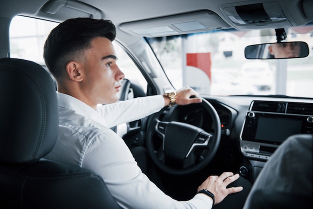 A young man sits in a newly purchased car at the wheel, a successful purchase.