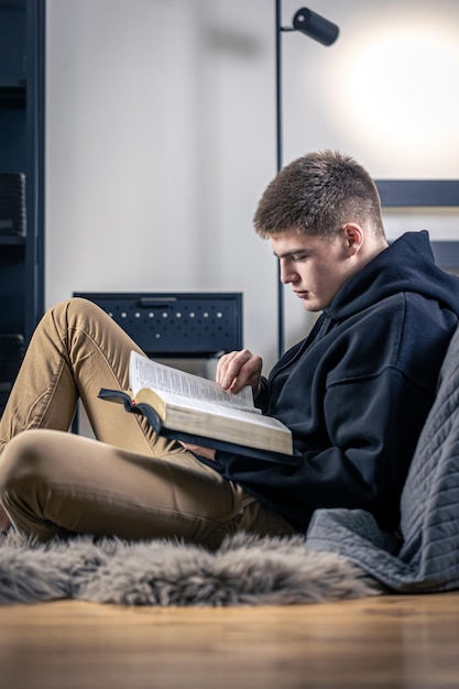Foto gratuita un giovane si siede in una stanza e legge la bibbia