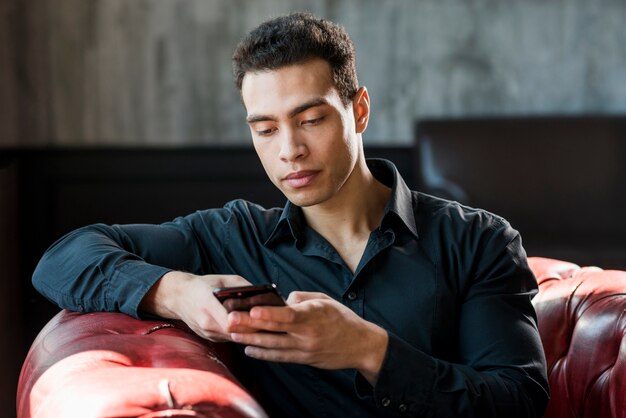 Free photo young man sitting on armchair using mobile phone