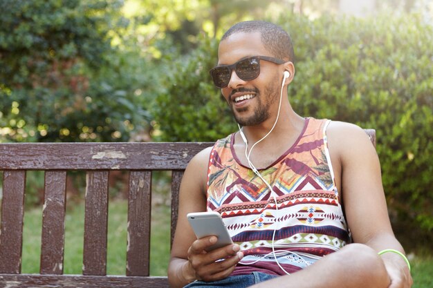 Young man sitting on bench in park and listening to music