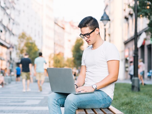 Young man sitting on bench using laptop