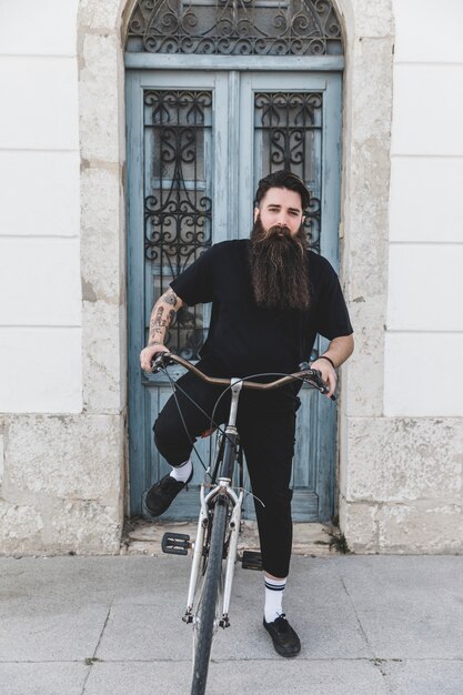 閉じた青いドアの前で自転車に座っている若い男