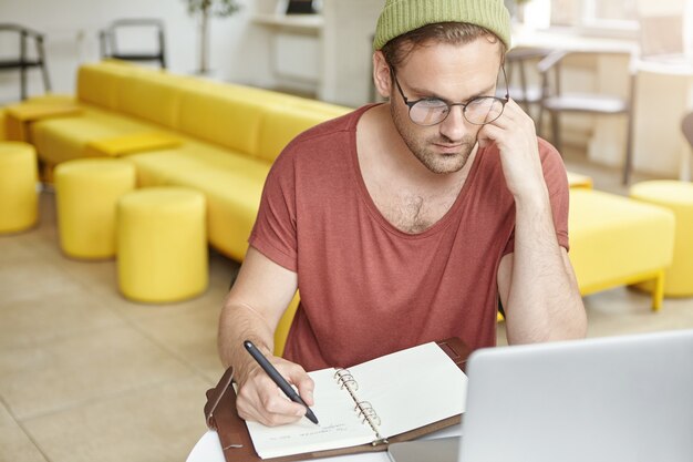 Giovane che si siede nella caffetteria con il computer portatile