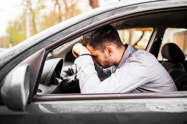 Young man sitting in car very upset and stressed after hard failure and moving in traffic jam