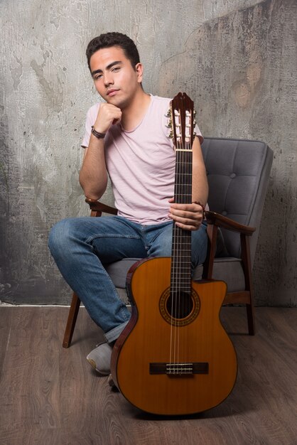 椅子に座ってギターを持っている若い男。高品質の写真