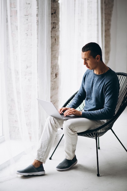 Free photo young man sitting in chair and using laptop