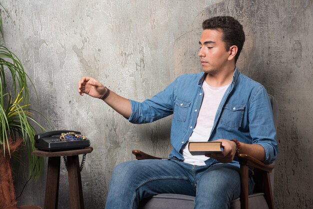 Young man sitting on chair with book on marble background. High quality photo