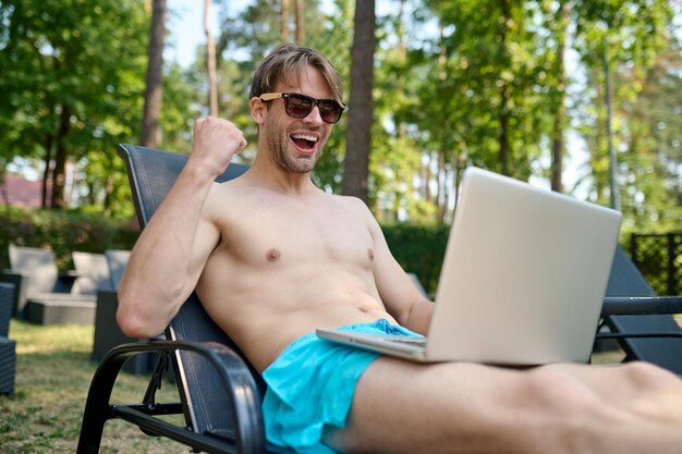 Free photo a young man sitting on a chaise longue with a laptop