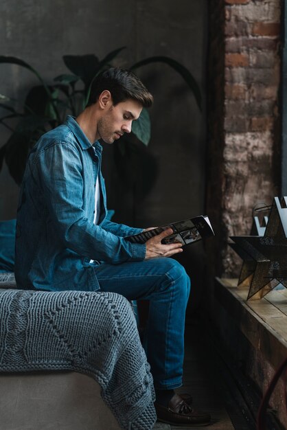 Young man sitting on couch reading magazine