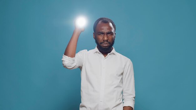 Young man sitting in the dark and holding flashlight to see, using lantern to search and do serious investigation. Active confident person with light looking around to find evidence. Night adventure