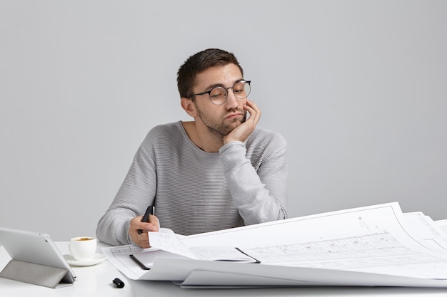 Foto gratuita giovane uomo seduto alla scrivania e fare il lavoro di ufficio