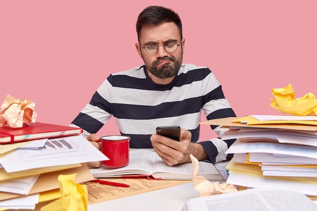 Young man sitting at desk with documents and holding phone