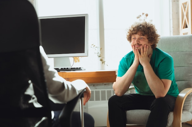 Young man sitting in office during the job interview with female employee, boss or HR-manager, talking, thinking, looks confident