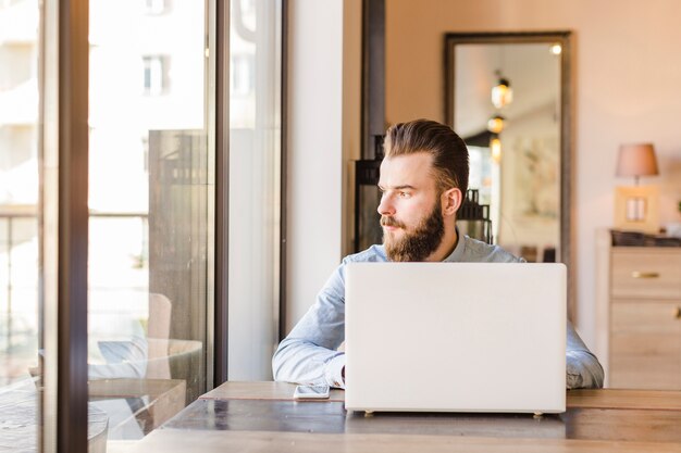 Young man sitting in restaurant with laptop and cellphone on desk