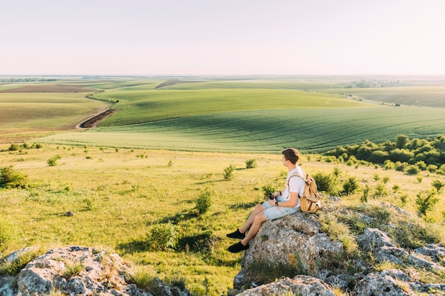 草原の風景を探索する岩に座っている若い男
