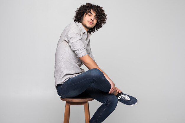 Young man sitting on a small stool against white wall