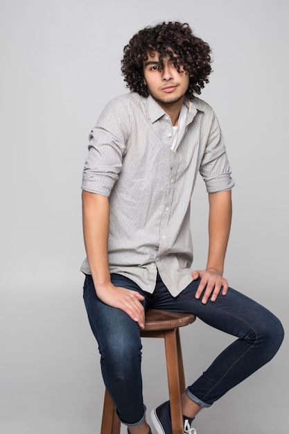 Young man sitting on a small stool against white wall