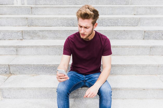 Young man sitting on staircase holding mobile phone