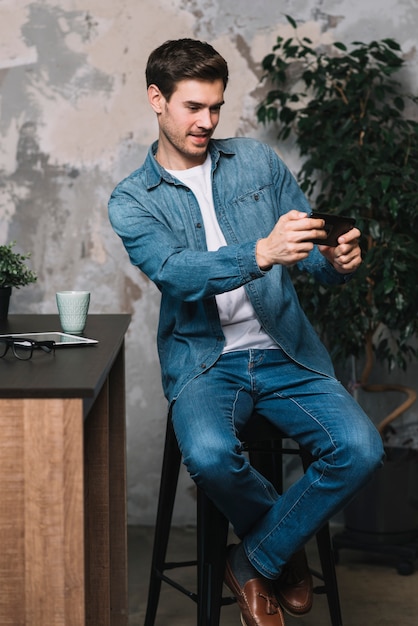 Free photo young man sitting on stool taking selfie through cellphone