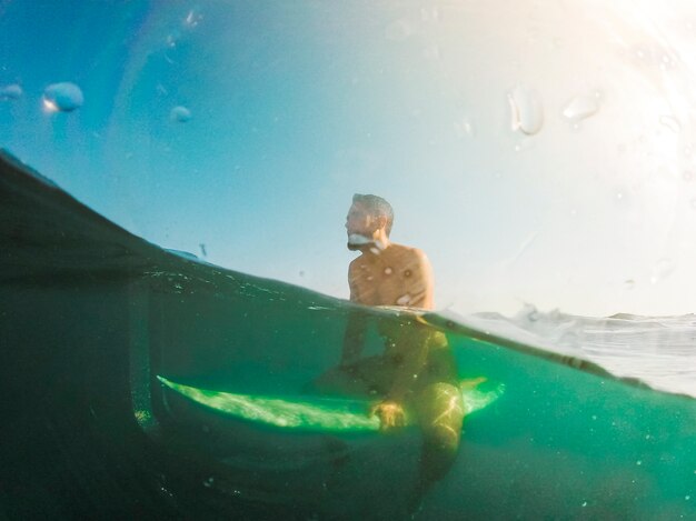 Young man sitting on surfboard in blue sea