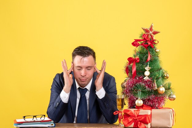 young man sitting at the table near xmas tree and presents on yellow