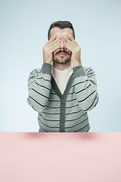 Young man sitting at table at  with eyes closed isolated on blue