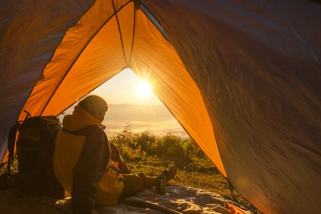 A young man sitting in the tent, looking at the mountain landscape in winter