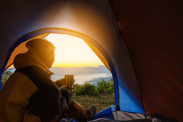 Молодой человек сидит в палатке с чашкой кофе