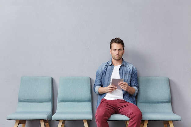 Young man sitting in waiting room holding tablet