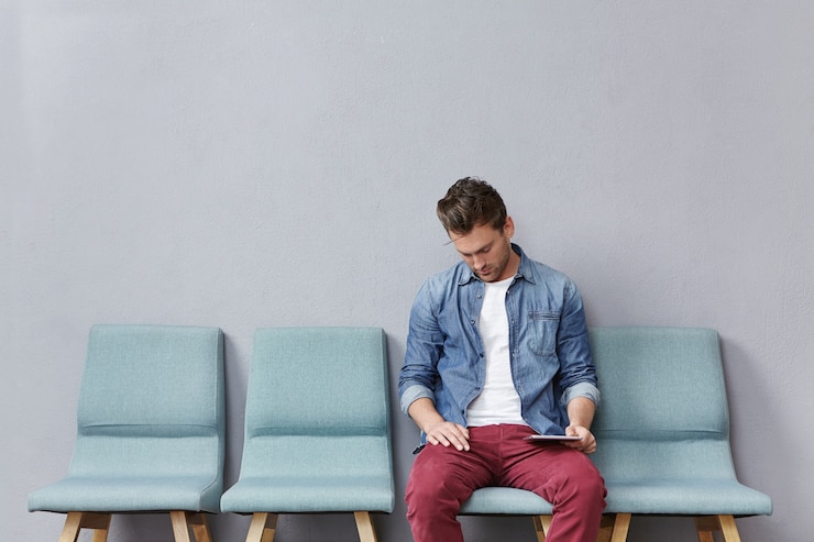 Young man sitting in waiting room holding tablet
