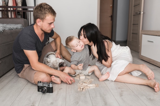 無料写真 木製のブロックで遊んでいる間に息子にキスをする彼女の妻を見て犬と一緒に座っている若い男