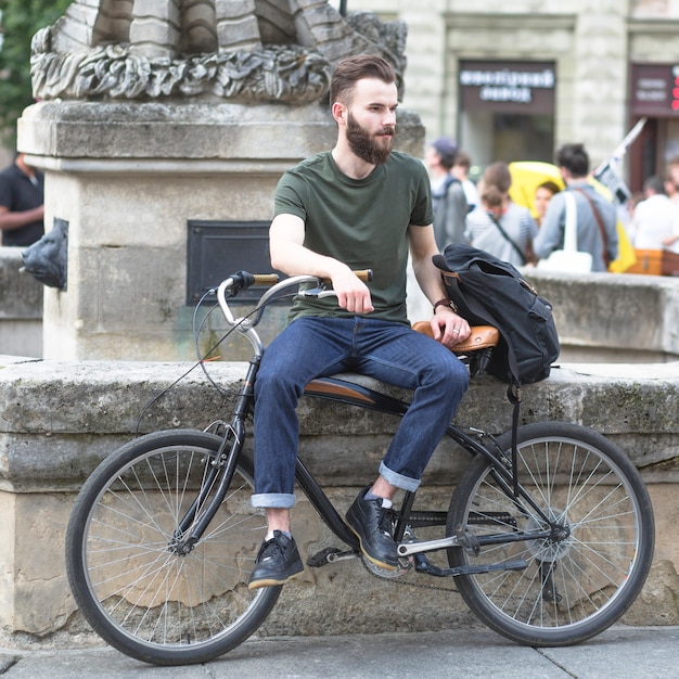 Foto gratuita giovane che si siede con la sua bicicletta all'aperto