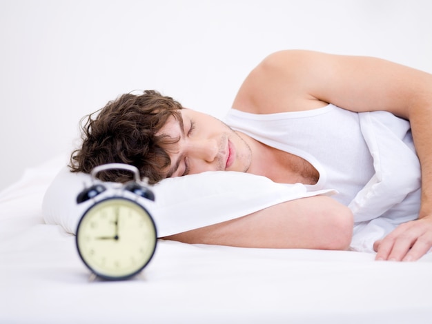 The young man sleeping with alarm clock near his head