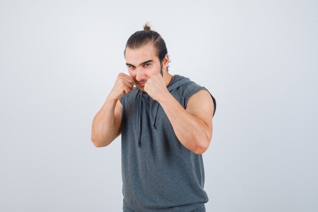 Young man in sleeveless hoodie standing in fight pose and looking confident , front view.