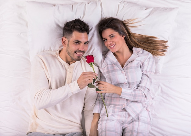 Young man smelling rose in bed with woman