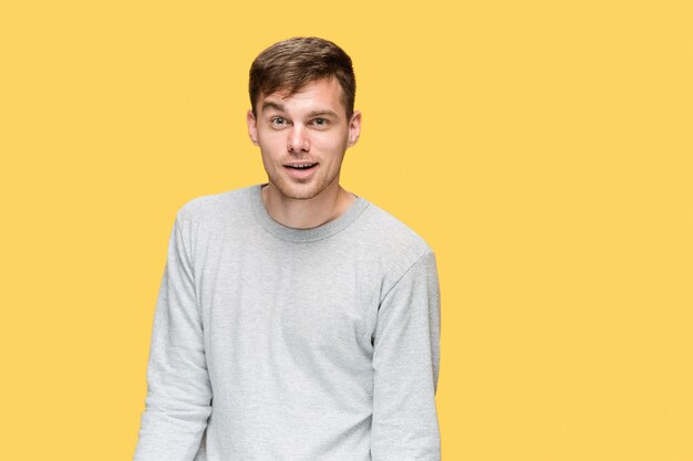 young man smiling and looking at camera on yellow studio background