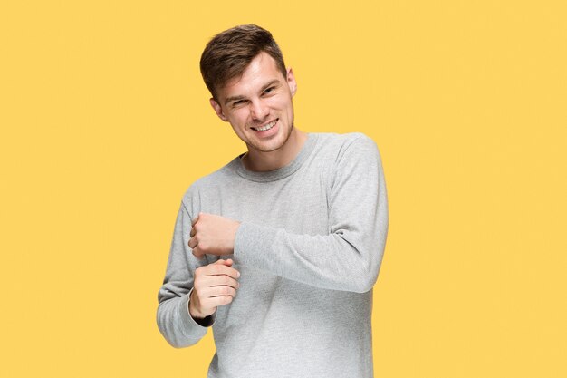 young man smiling and looking at camera on yellow studio background