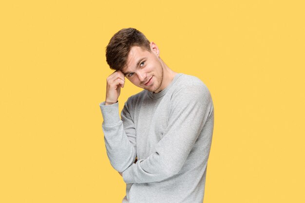 young man smiling and looking at camera on yellow studio background