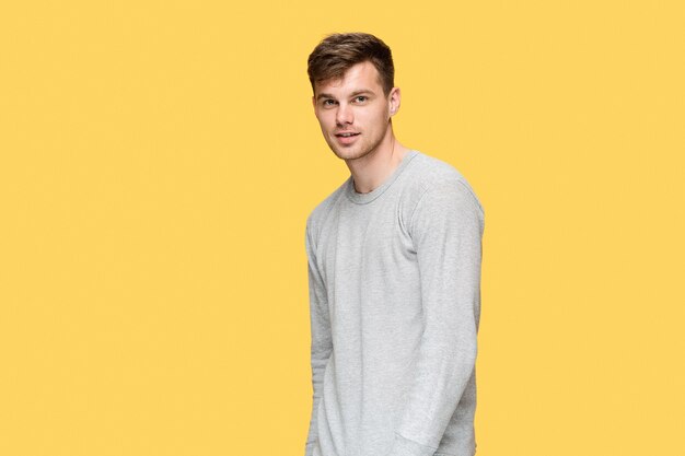 young man smiling and looking at camera on yellow studio background