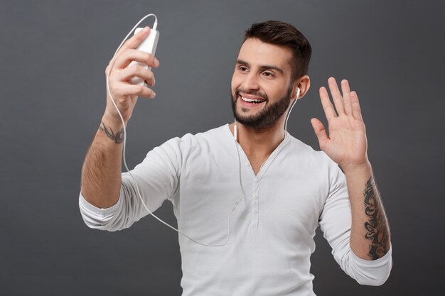 Young man smiling looking at phone greeting over grey wall