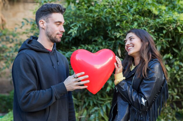 Young man and smiling woman with balloon in form of heart 