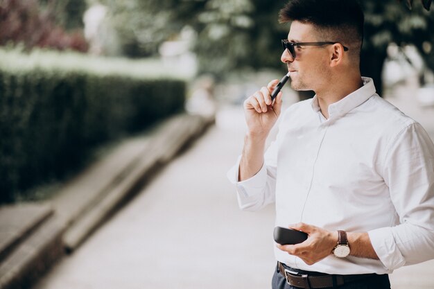 Young man smoking electro cigarette outside in park