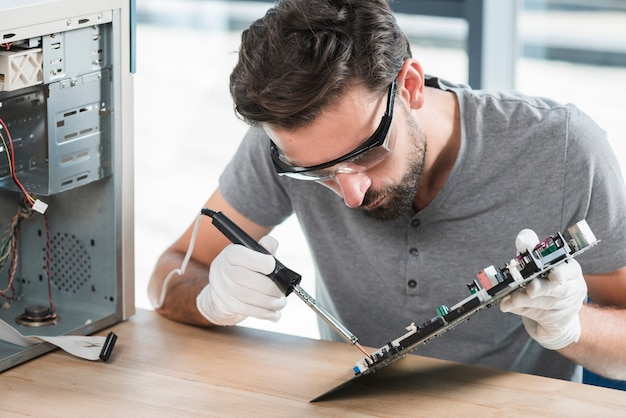 Young man soldering computer circuit over wooden desk