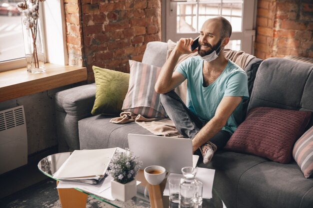 Young man speaking on the phone at home while being quarantine and freelance working