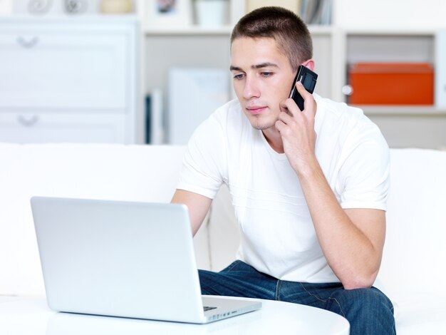Young man speaks on the phone and works on the laptop